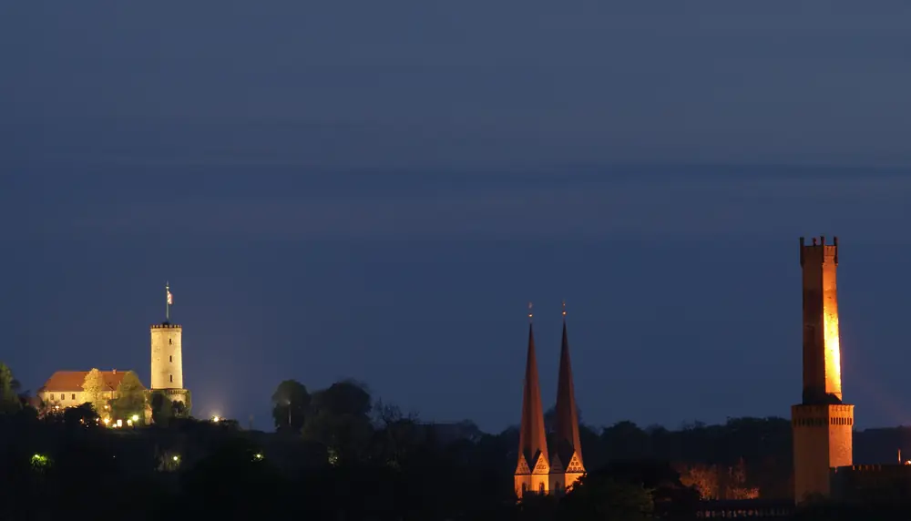 Bielefeld bei Nacht: links die beleuchtete Sparrenburg, in der Mitte die Türme der Neustädter Marienkirche, rechts der Schornstein der Ravensberger Spinnerei